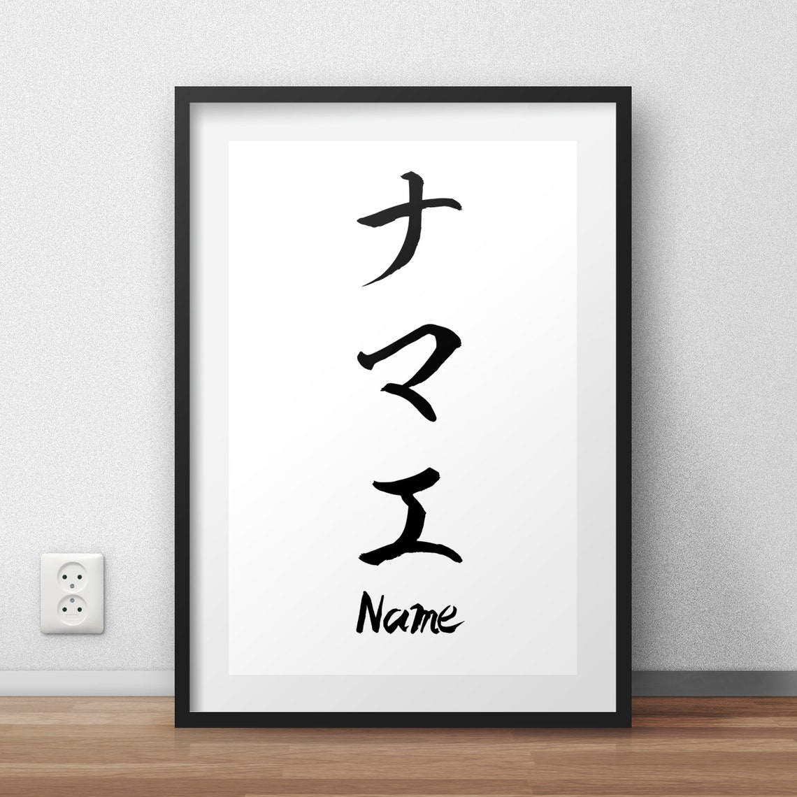 Un cadre posé contre un mur : trois katakana calligraphiés au pinceau, ナマエ (namae), le mot japonais pour « nom ».