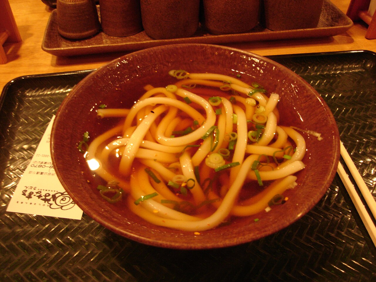 Un bol d'udon : d'épaisses nouilles blanches dans un bouillon brun, avec de la ciboule émincée