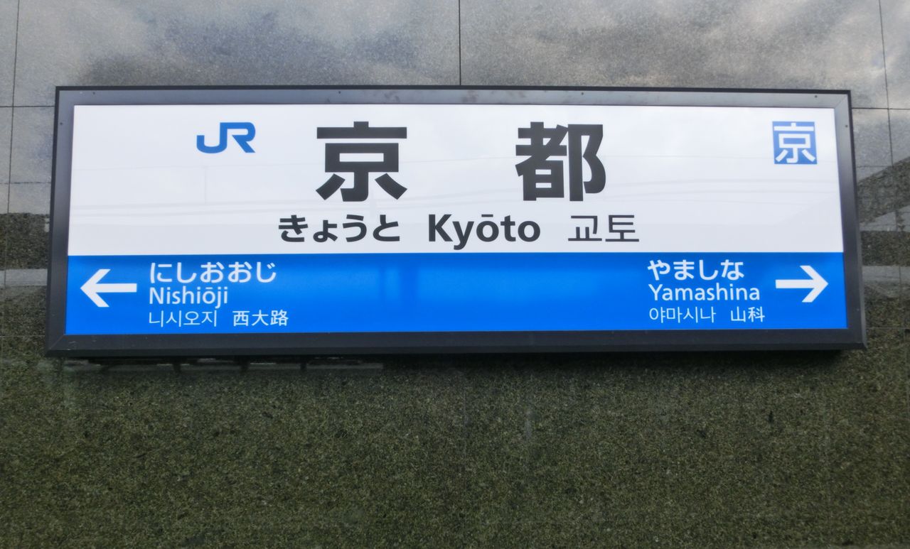 Panneau de la gare de Kyoto : le nom écrit en hiragana, きょうと, et juste à côté en romaji, « Kyōto », avec une barre sur le premier o
