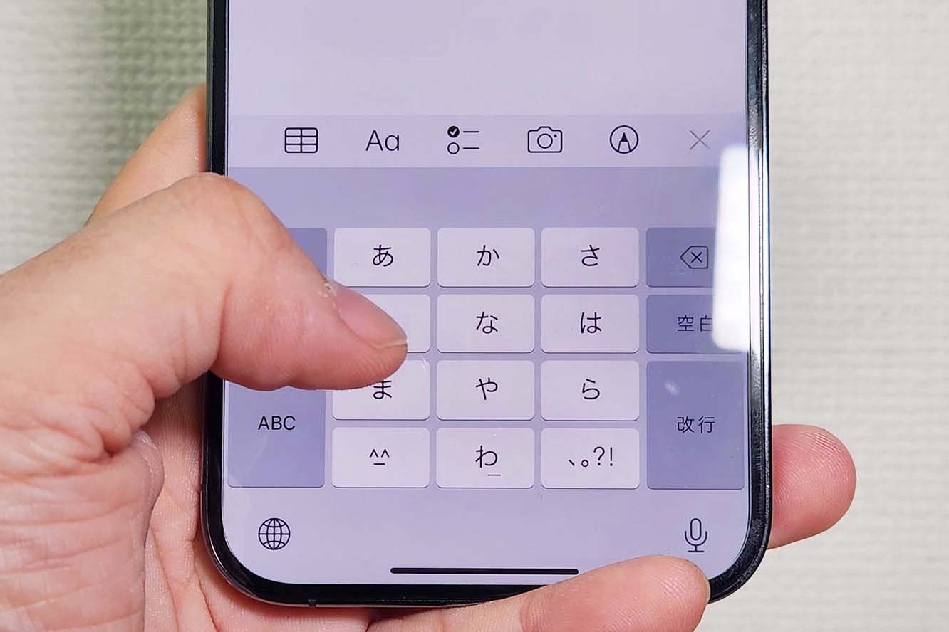 Un pouce posé sur le clavier kana d'un iPhone, avec ses touches あ, か, さ, た, な, は, ま, や, ら et わ