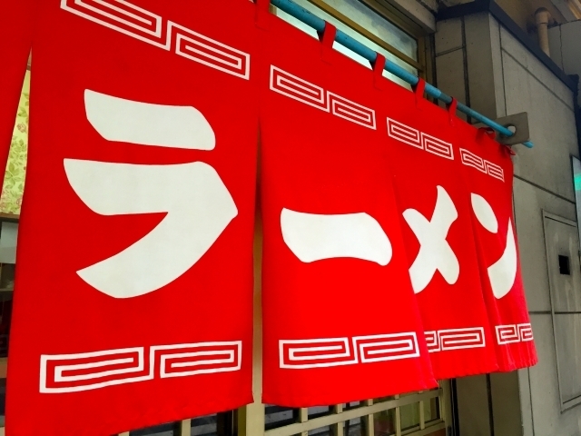 Rideau rouge à l'entrée d'un restaurant, avec le mot ラーメン écrit en blanc sur plusieurs pans