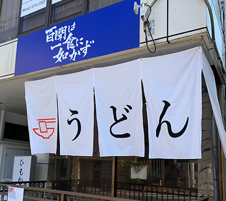Devanture d'un restaurant avec un rideau blanc où うどん est écrit en grands hiragana noirs